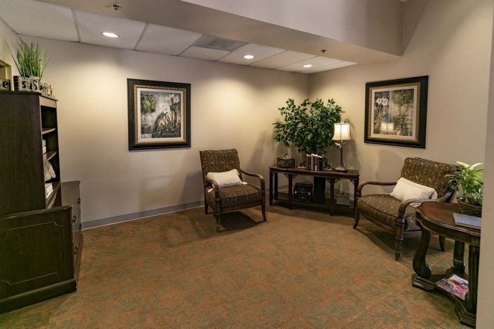 A cozy waiting room with comfortable chairs, framed artwork, and a potted plant.