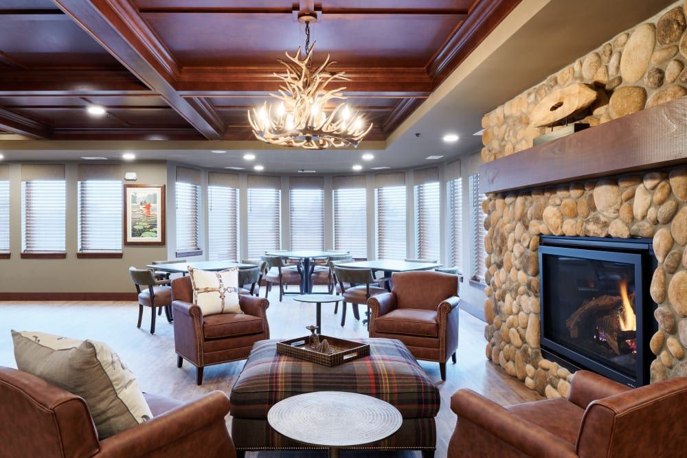 A cozy living room featuring a modern design with leather chairs, a stone fireplace, and a decorative chandelier.