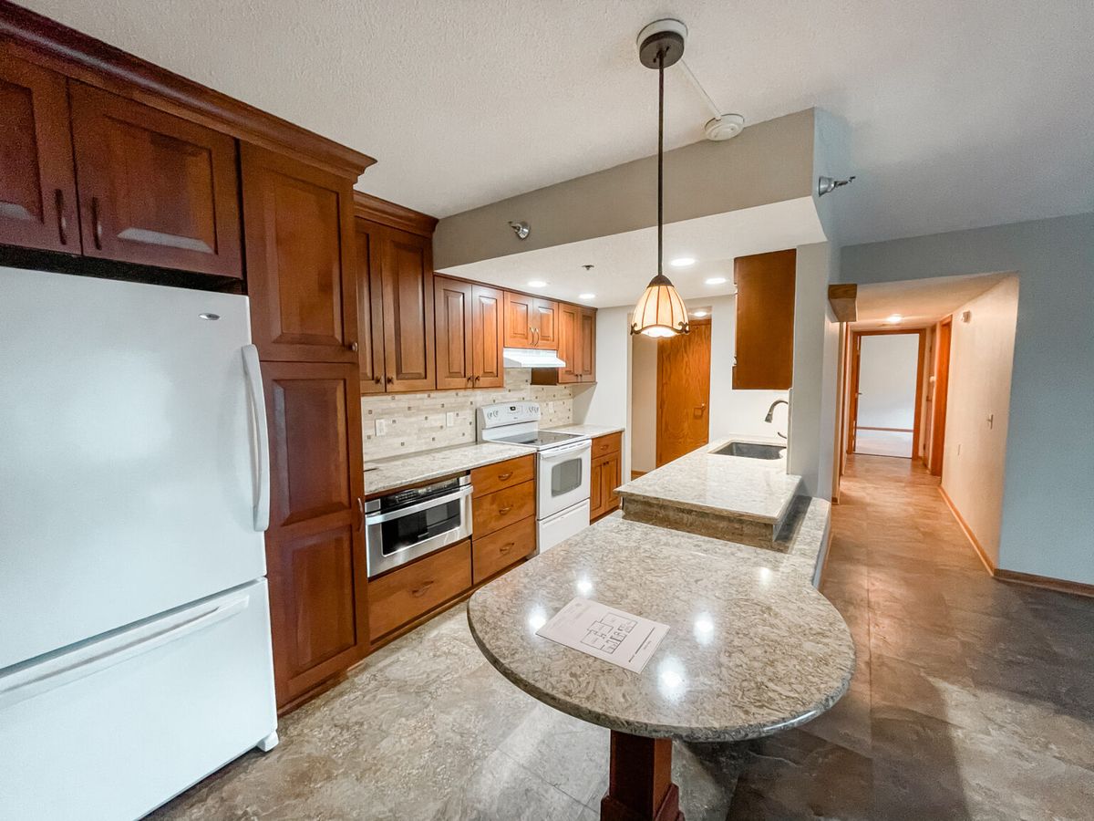 A modern kitchen featuring wood cabinets, marble countertops, and sleek appliances.