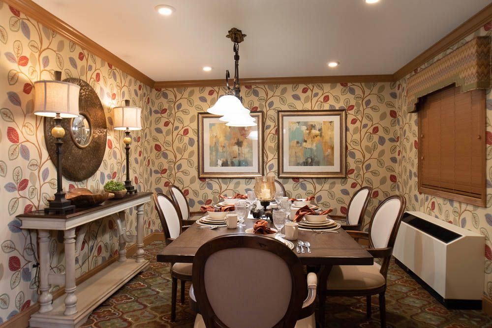 An elegantly decorated dining room with a large table set for a meal, featuring classic chairs, artistic wall decor, and a central chandelier.