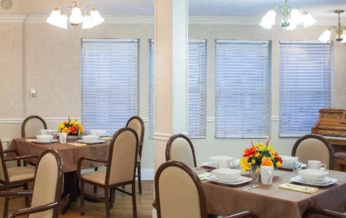 A well-lit dining room with neatly arranged tables and chairs, decorated with flowers and set for a meal.