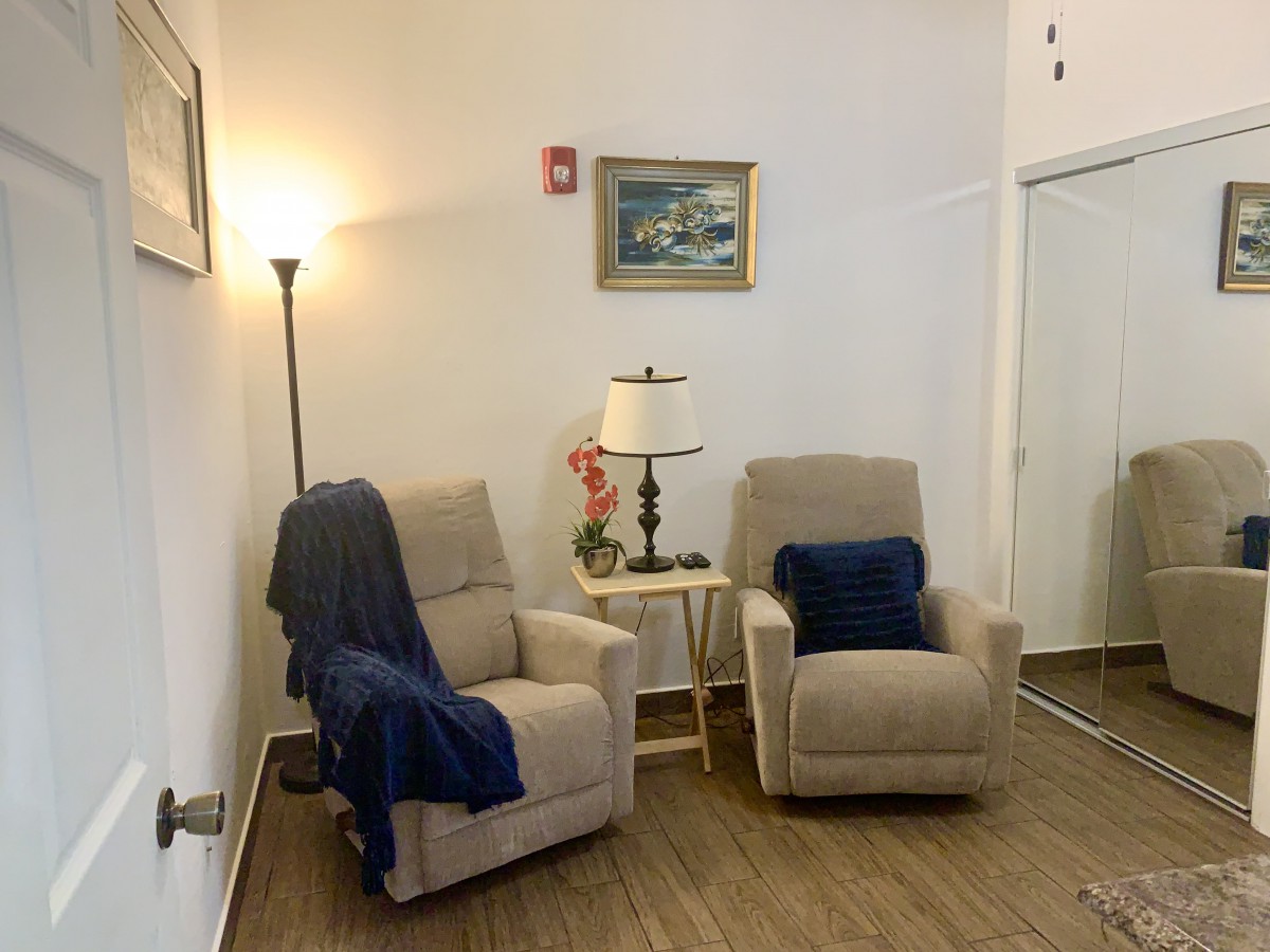 A cozy living room corner with two beige recliner chairs, a floor lamp, and a small table adorned with a table lamp and decor.