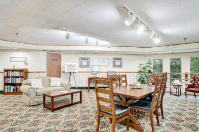 A well-lit conference room featuring a large table with wooden chairs, a comfortable sofa, and decorative indoor plants.