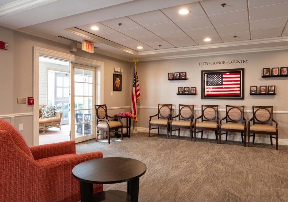 A waiting room with multiple chairs, an American flag displayed on the wall, and a small coffee table in the center.