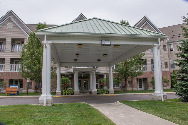 A building entrance with a large canopy supported by columns and a concrete pathway leading to the doors.