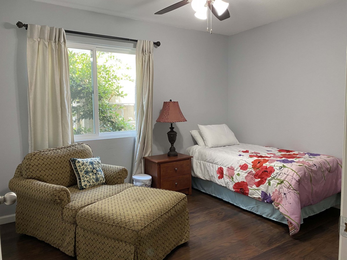 A cozy bedroom with a single bed, an armchair, and natural light from a window.