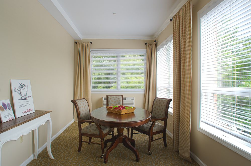 A cozy dining area with a round table and chairs by large windows with beige curtains.