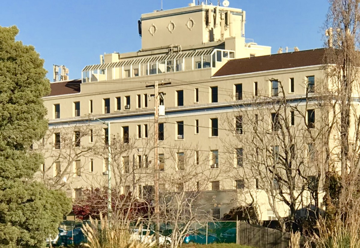 A large multi-story hospital building surrounded by trees under a clear blue sky.