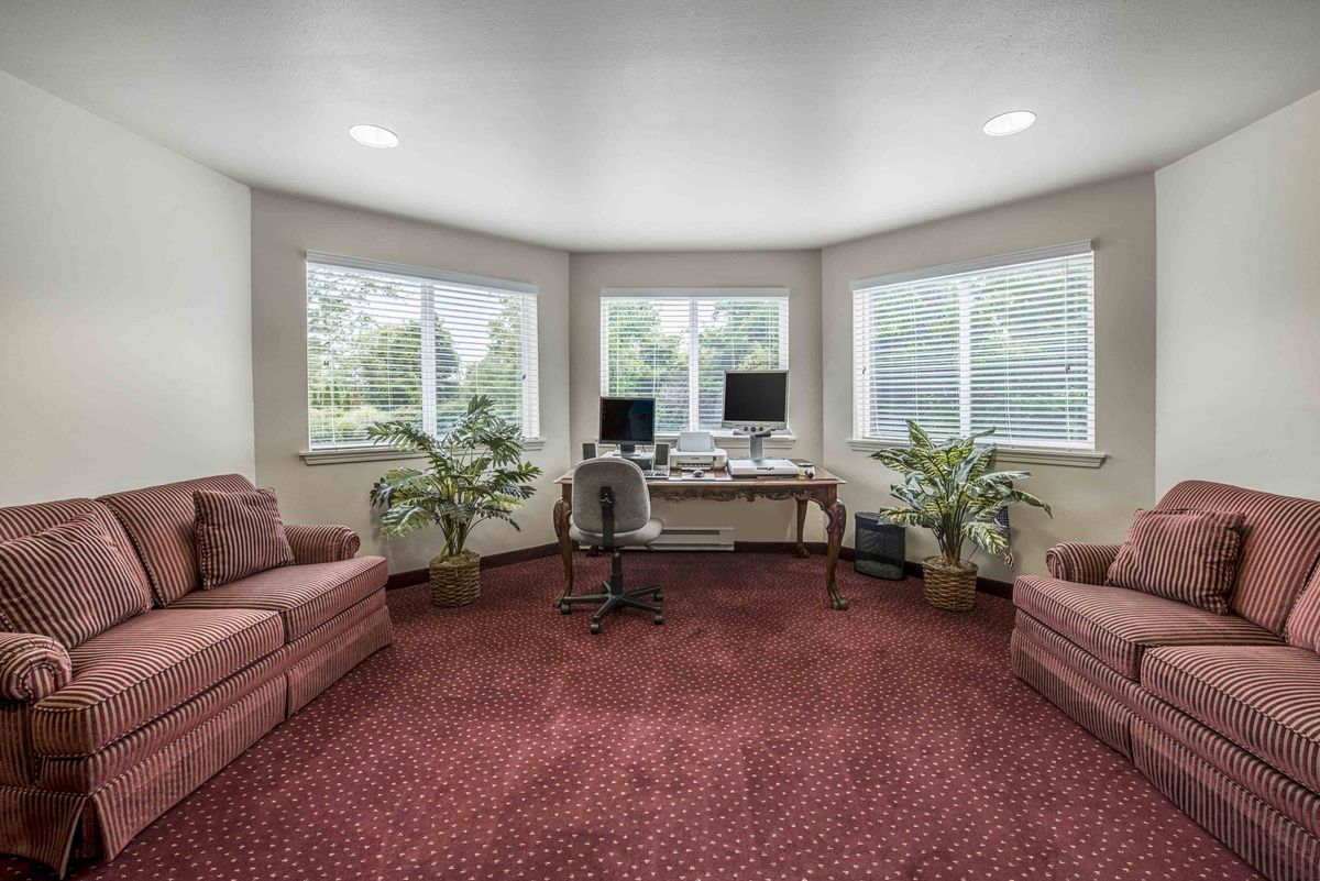 A spacious home office with a desk, computer, and comfortable seating surrounded by natural light from large windows.