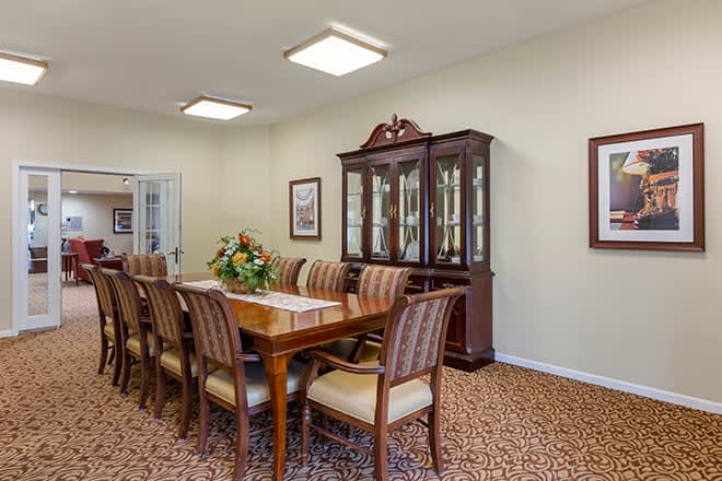 A formal dining room with a long wooden table, surrounded by upholstered chairs and a glass-front cabinet.