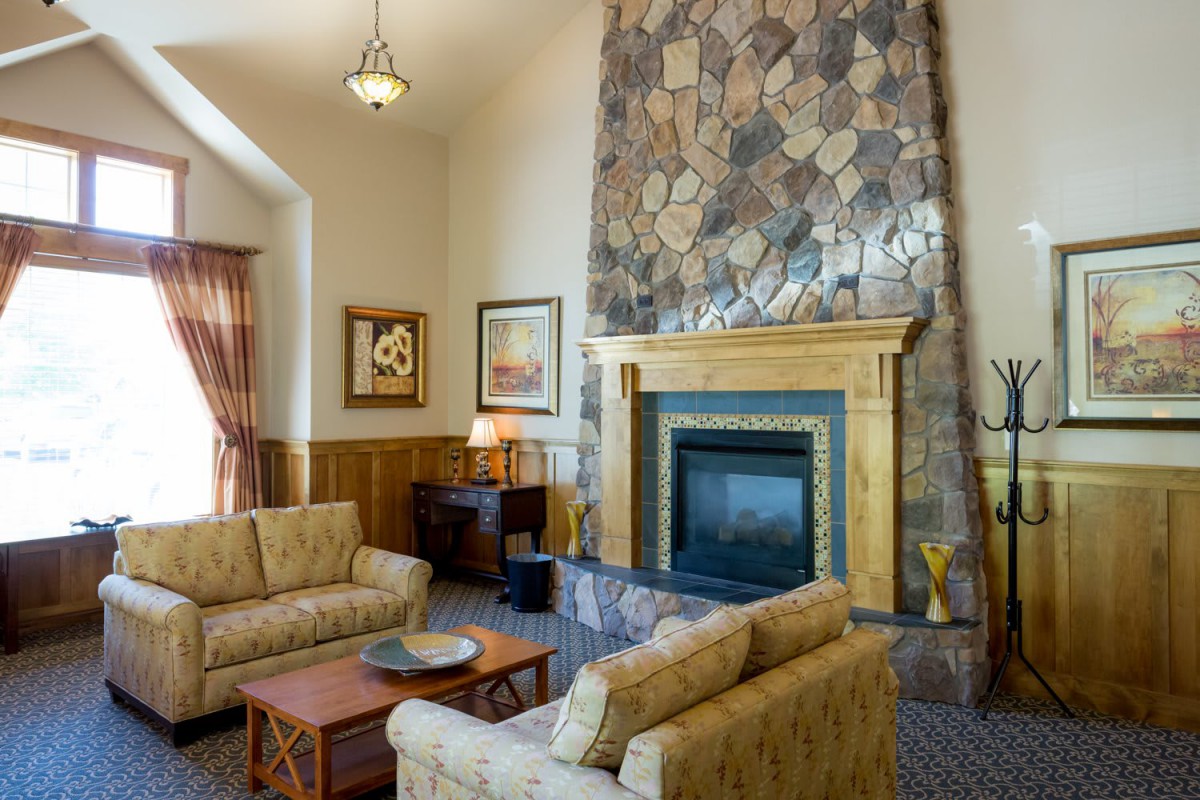 A cozy living room featuring a stone fireplace, comfortable couches, and warm wood paneling.