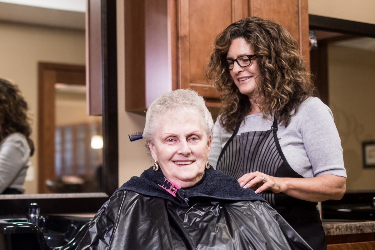 A senior woman getting her hair styled at a salon, smiling with her hairdresser.