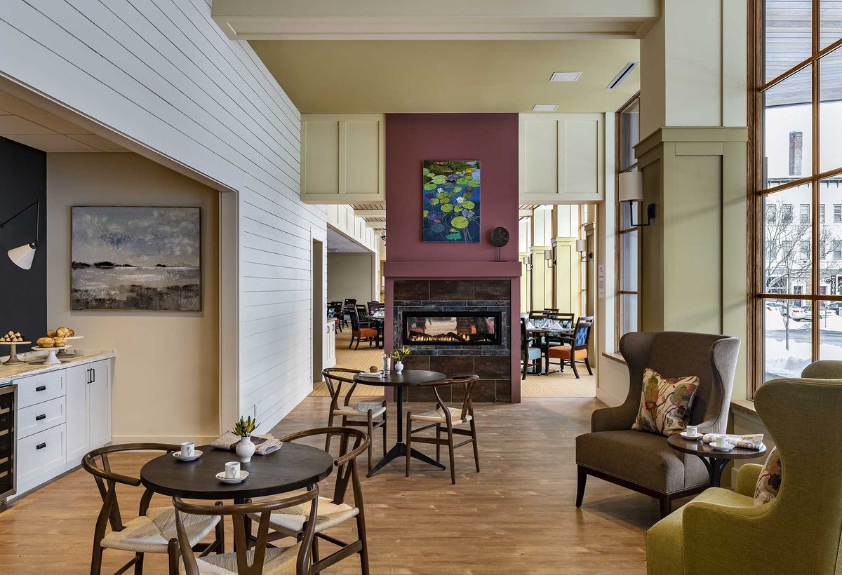 A cozy lounge area featuring a fireplace surrounded by comfortable seating and tables, with artwork adorning the walls.