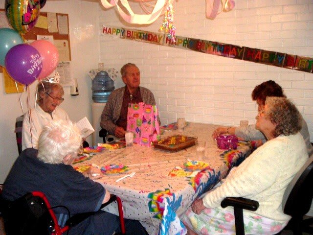 A group of seniors celebrating a birthday with decorations and gifts around a table.