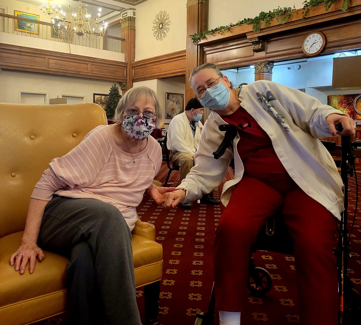 Two women wearing masks sitting together in a nursing home.
