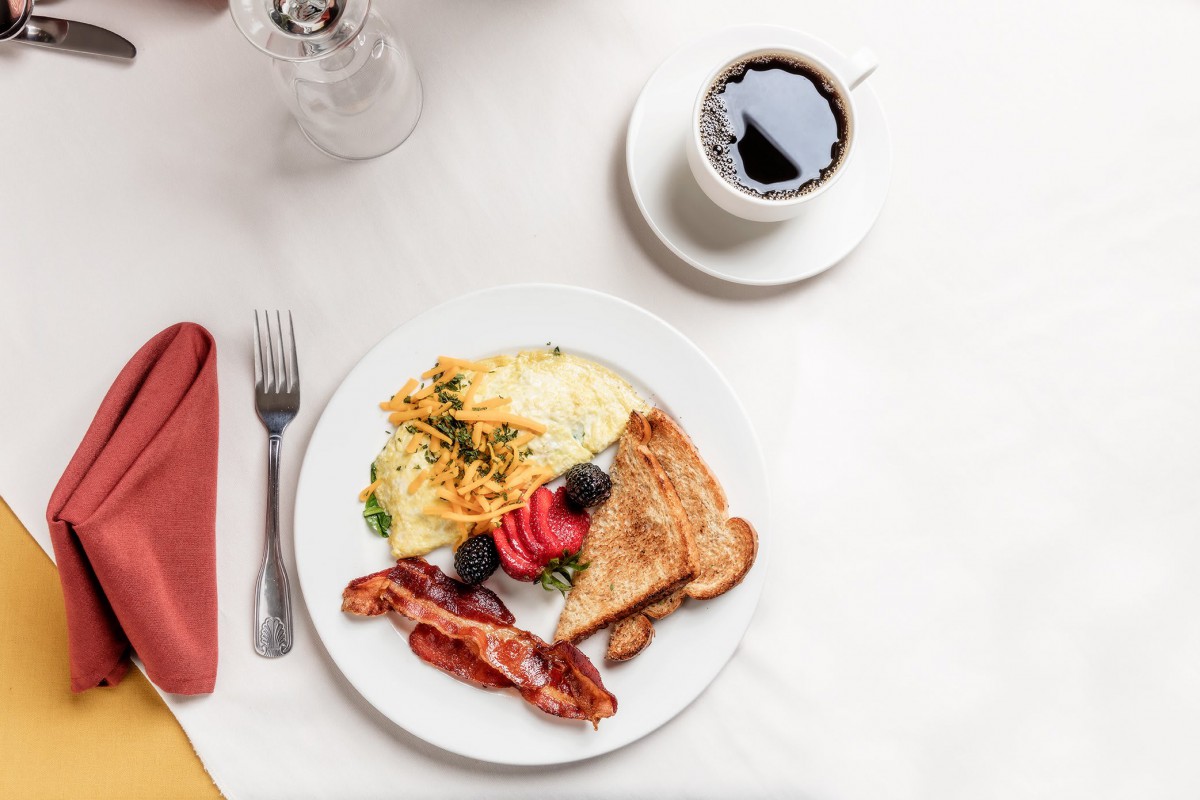 A delicious breakfast plate with scrambled eggs, bacon, toast, and a cup of coffee.