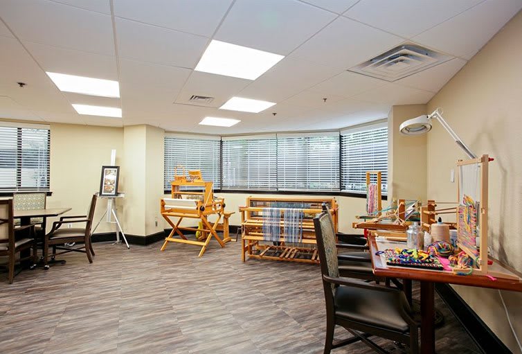An art studio with looms and crafting supplies, featuring large windows and spacious seating.