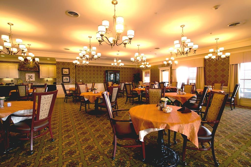 A warmly lit dining area with neatly arranged tables and elegant chandeliers.