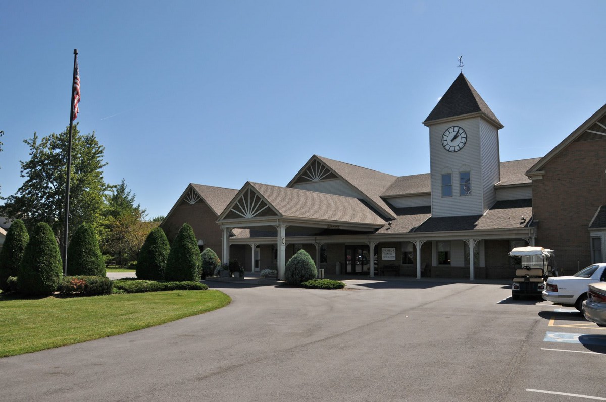 A large clock tower building with a spacious driveway and surrounding greenery.