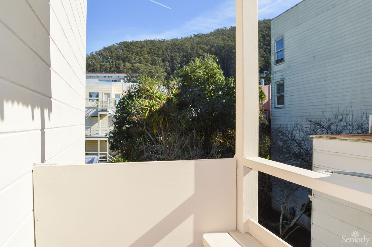 A scenic balcony view featuring lush greenery and adjacent buildings under a clear blue sky.