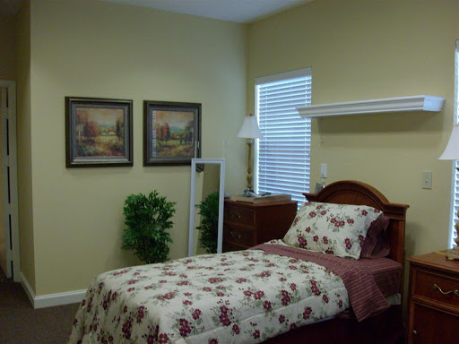 A cozy bedroom featuring floral bedding, decorative paintings, and warm wall colors.