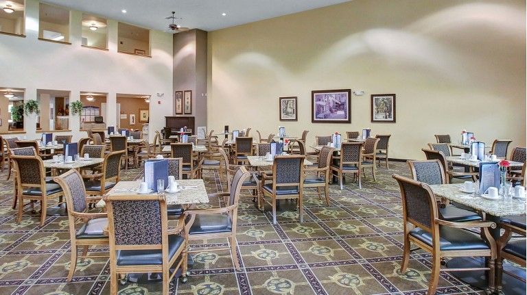 A spacious dining area with neatly arranged tables and chairs, featuring a patterned carpet and wall decorations.