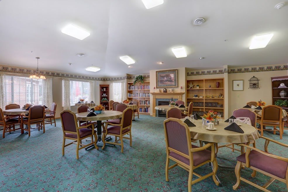 A cozy dining area with round tables, chairs, a fireplace, and bookshelves.