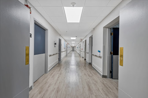 A clean and well-lit hospital corridor with multiple doors along the sides.