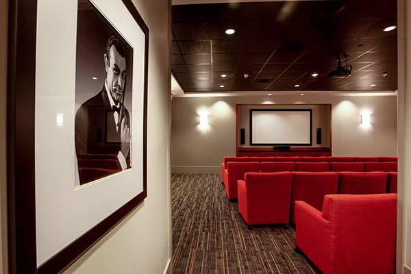 A cozy home theater setup with red seats and a large screen, featuring a framed picture on the wall.