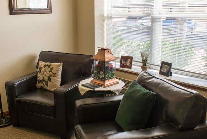 A cozy living room with dark leather sofas, decorative cushions, and a table lamp near the window.