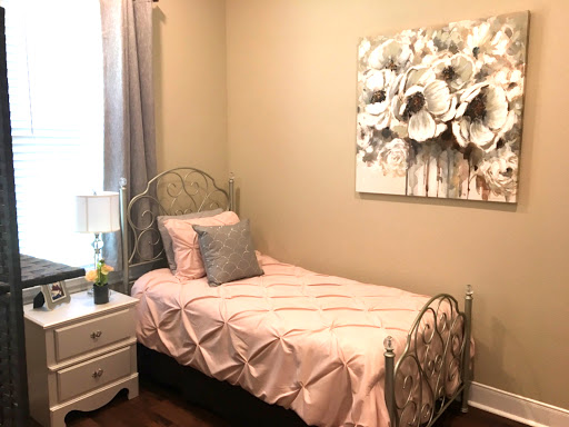 A cozy and elegantly designed bedroom featuring a single bed with pink bedding, complemented by floral wall art and a stylish nightstand.