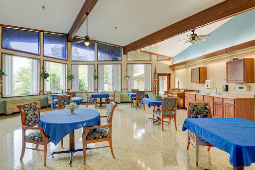A spacious and airy dining area featuring blue tablecloths, natural light streaming in through large windows, and a welcoming atmosphere.