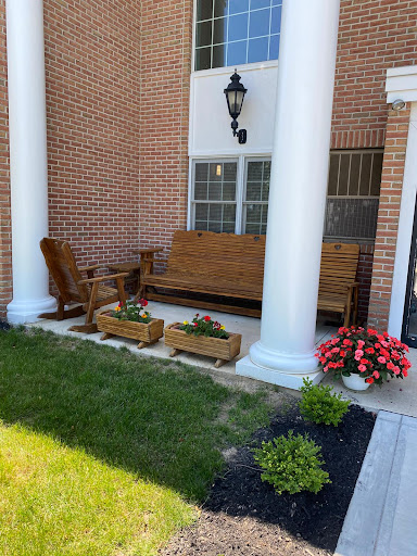 A cozy outdoor porch area featuring a wooden bench and chairs, surrounded by colorful flower arrangements and sturdy columns.