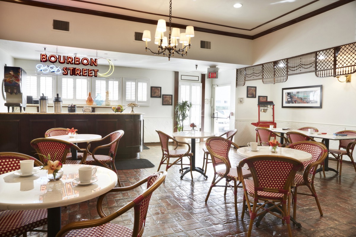 A cozy restaurant interior with elegantly arranged tables and chairs, featuring a chandelier and warm decor.