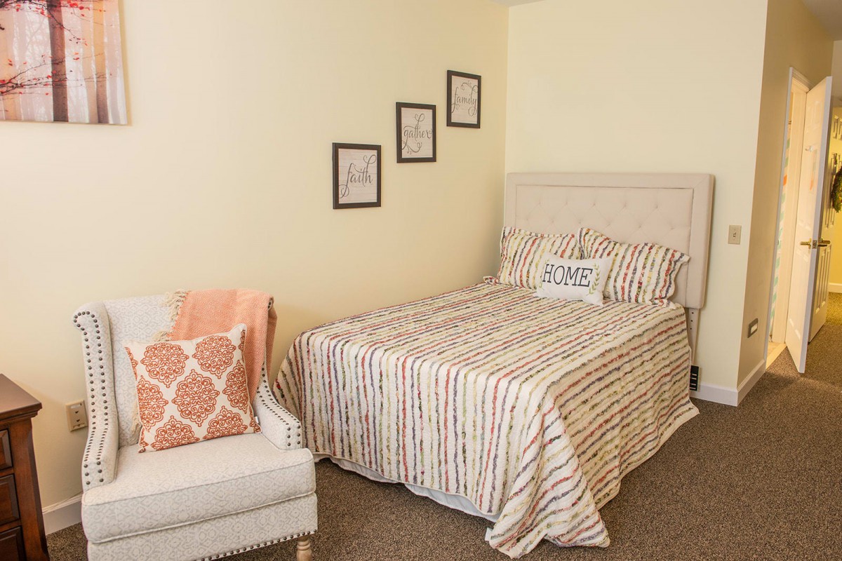 A cozy bedroom with a striped bedspread and decorative pillows, accompanied by wall art and a comfortable chair.