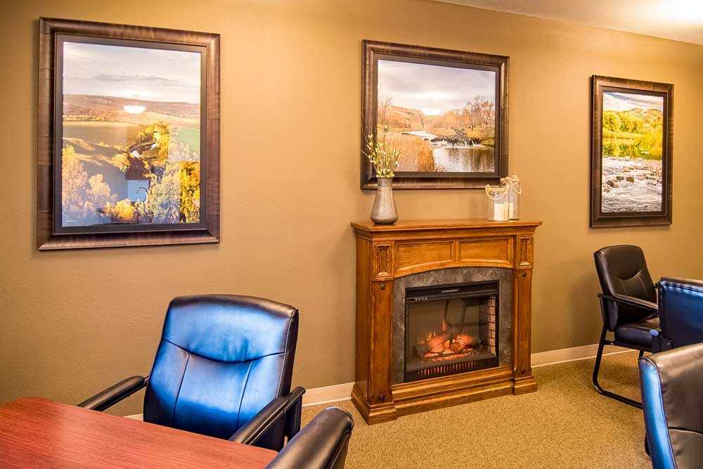 A cozy office interior with a decorative fireplace and framed artwork.