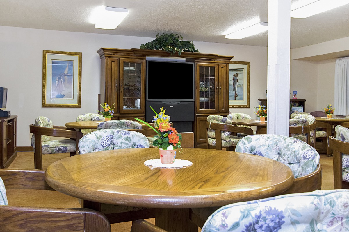 A cozy dining area with a wooden table, floral chairs, and a television in a wooden cabinet.