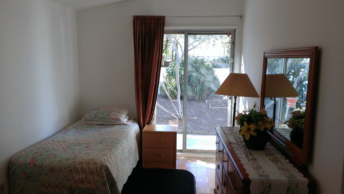 A cozy bedroom with a single bed, dresser, and a large window overlooking the garden.