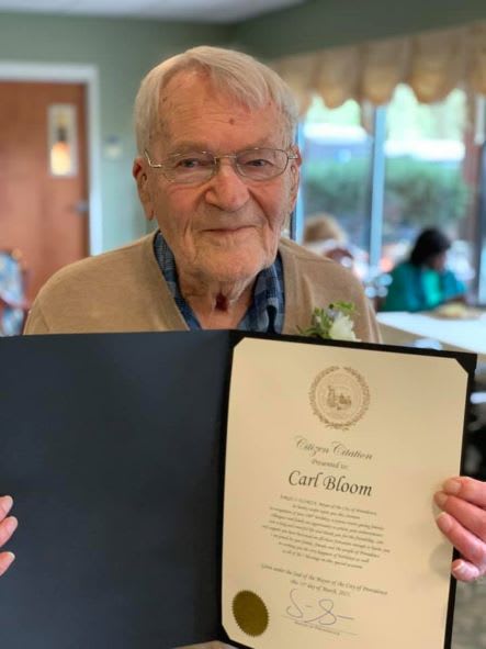 An elderly man proudly holding a certificate, smiling indoors.