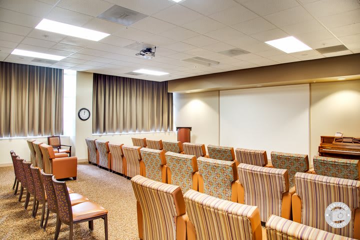 An empty conference room with a podium and arranged seating facing a projector screen.