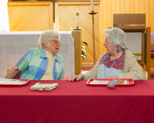 Two elderly women engaged in a lively conversation over a meal at a community gathering.
