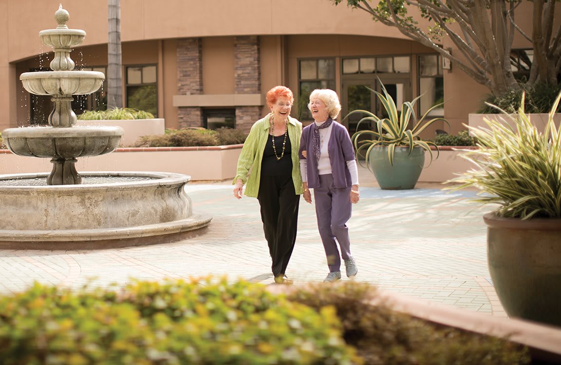 Two elderly women walking together in a courtyard, enjoying each other's company.