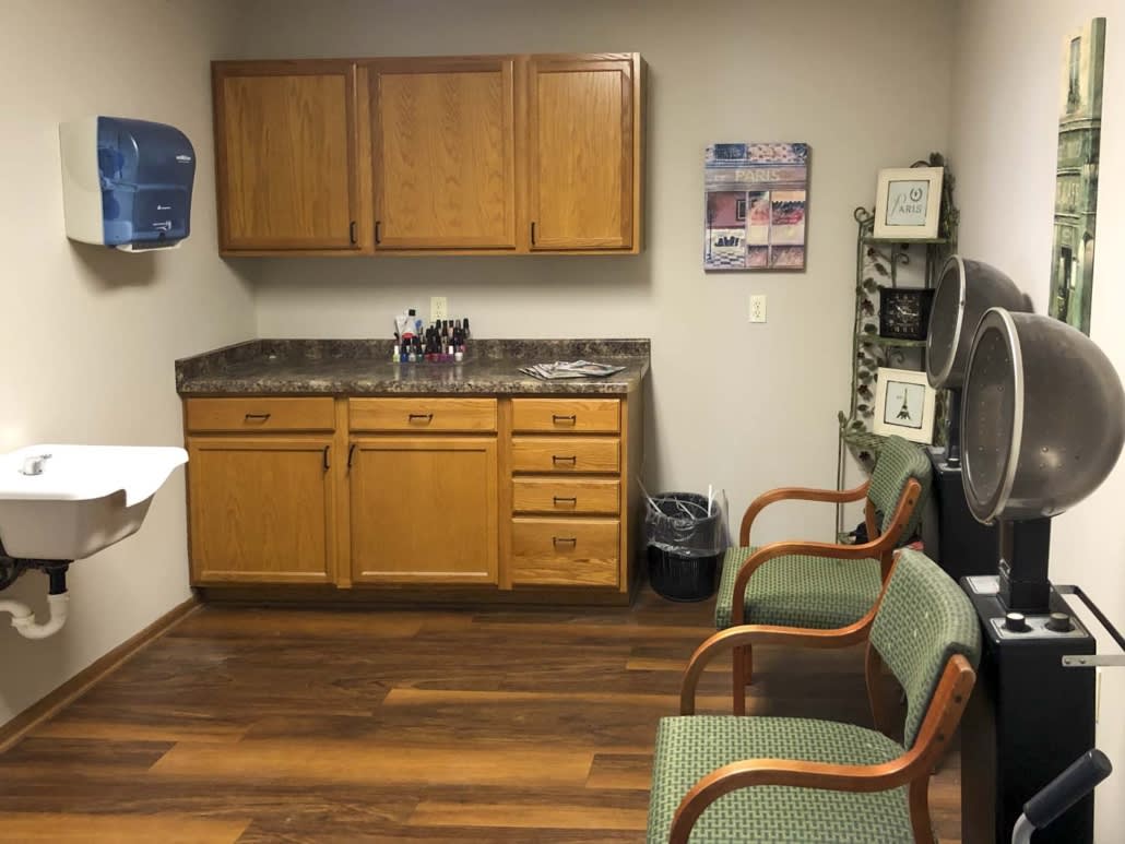 An office waiting room with wooden cabinets, a sink, and chairs arranged on a wooden floor.