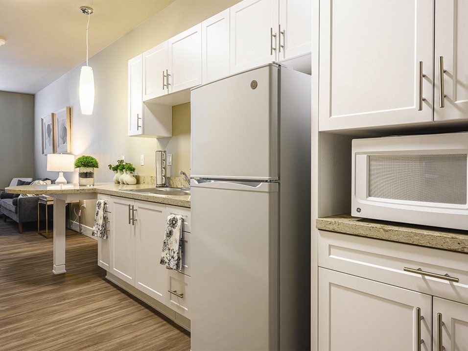 A modern kitchen featuring white cabinetry and stainless steel appliances, including a refrigerator and microwave.