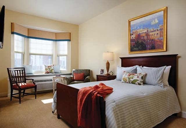 A cozy bedroom with a neatly made bed, armchair, and window view.