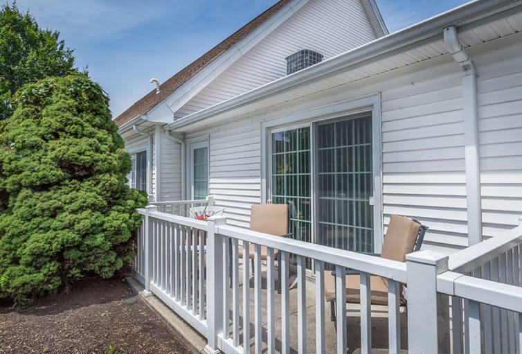 A cozy patio with chairs and a white railing outside a house.