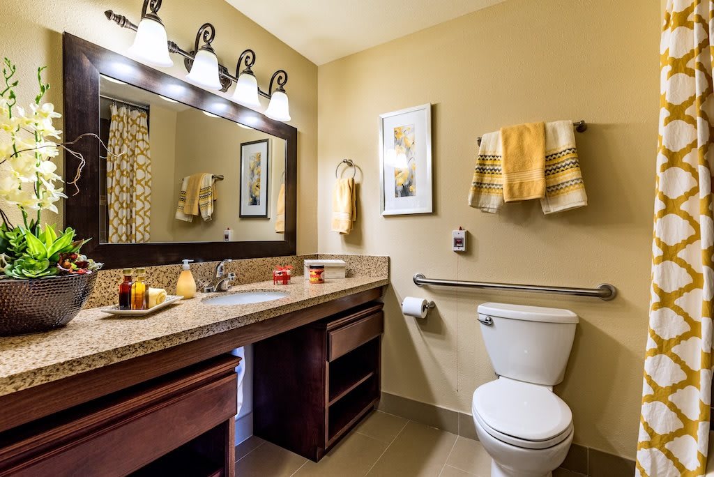 A well-lit bathroom with a large mirror, sink, and neatly arranged towels.