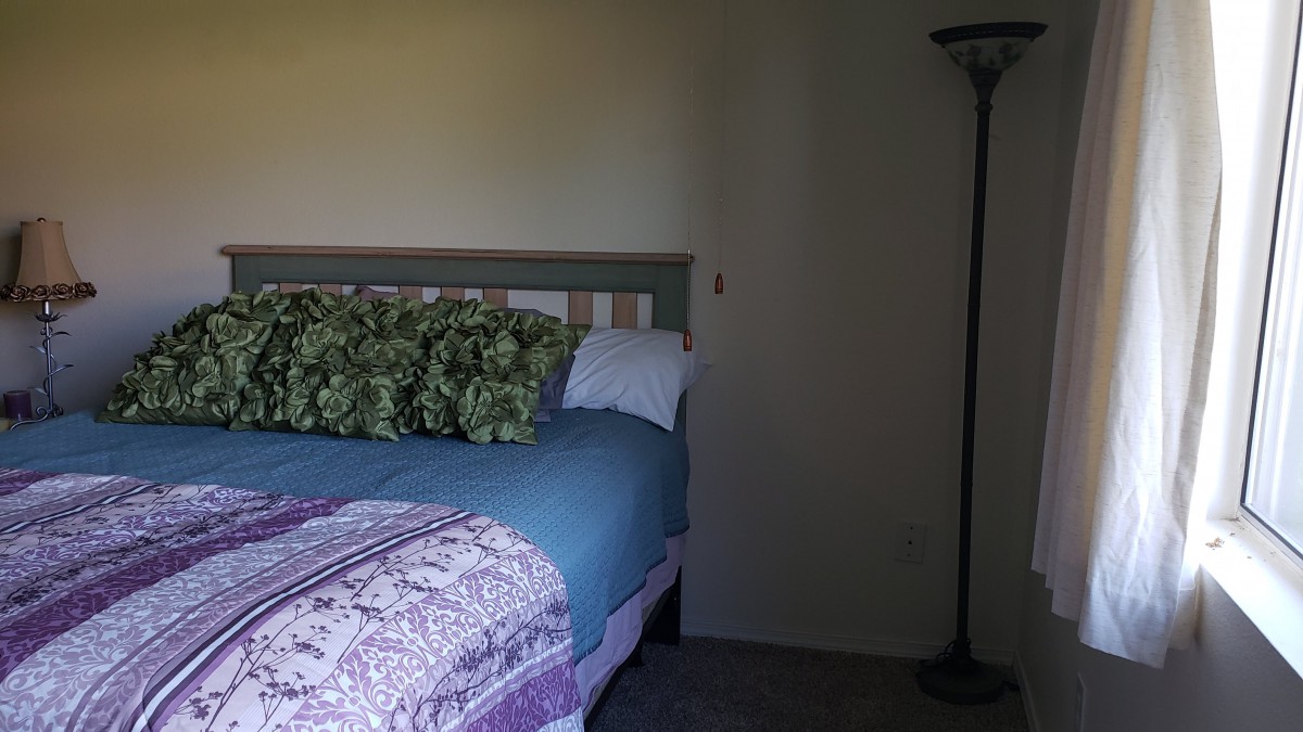 A cozy bedroom with a neatly made bed, adorned with patterned pillows and a floor lamp beside it.