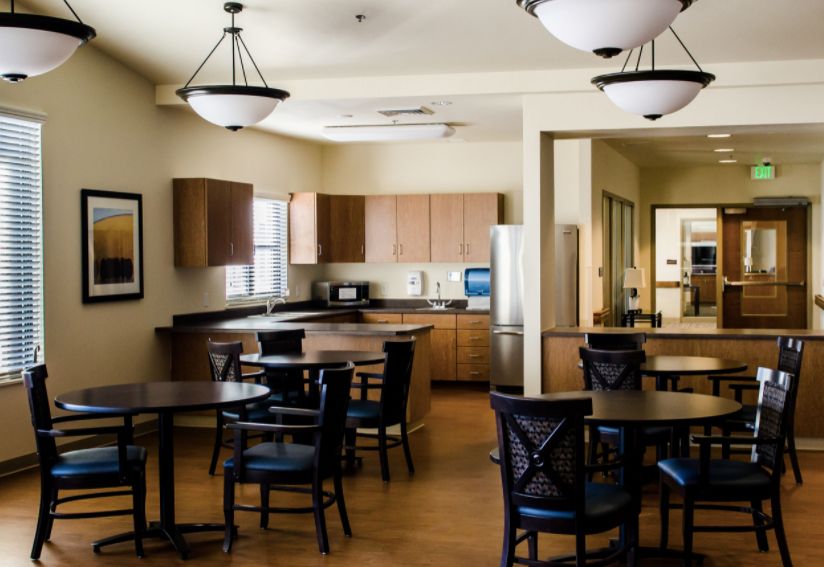 A modern kitchen and dining area featuring wooden cabinets, a stainless steel fridge, and multiple tables with chairs.