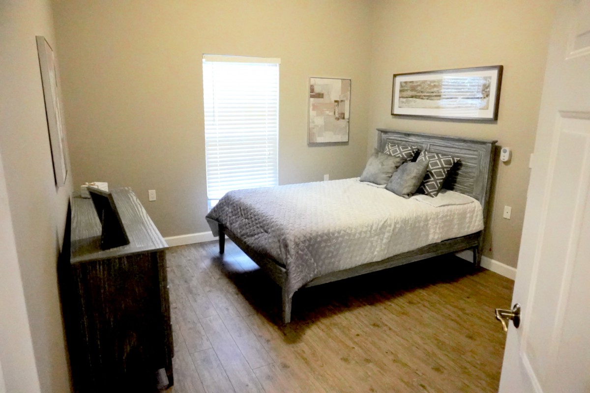 A cozy bedroom with a neatly made bed, wooden floors, and simple decor.